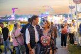 Ein Paar schlendert bei Sonnenuntergang verliebt über den Viehmarkt, die Frau trägt ein Lebkuchenherz um den Hals.