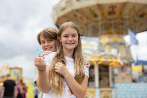 Zwei Kinder halten Fahrchips in der Hand und freuen sich auf die bevorstehende Fahrt mit dem Kettenkarussell